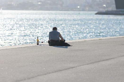 A lonely man drinking wine from a glass at the waterfront. Mid shot