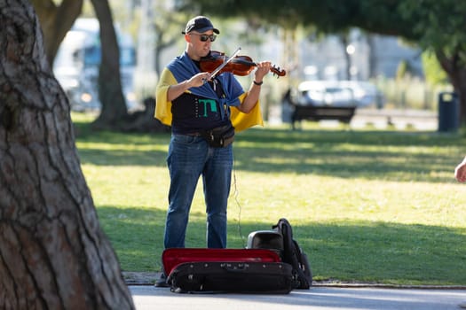 11 April 2023 Lisbon, Portugal: a man with a Ukrainian flag on his shoulders plays a violin in the street. Mid shot