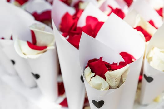 White and red rose petals wrapped in paper bouquet for a wedding.