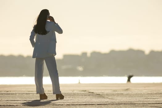 A business woman on the waterfront talking on the phone at sunset. Mid shot