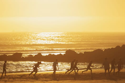 Young people playing ball on the beach at sunset. Mid shot