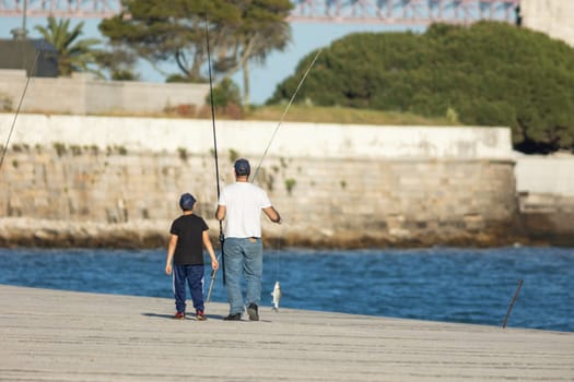 Father and son walking along the pier holding fish hanging on a fishing line. Mid shot