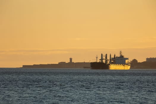 An industrial ship sails down the river at sunset. Mid shot