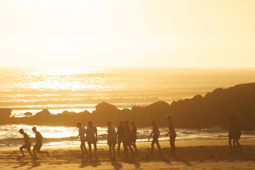 Young men playing a ball on the beach at sunset. Mid shot