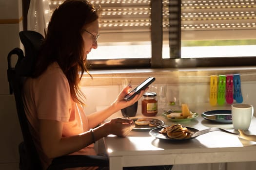 An adult business woman eats pancakes for breakfast and looks at her phone. Mid shot