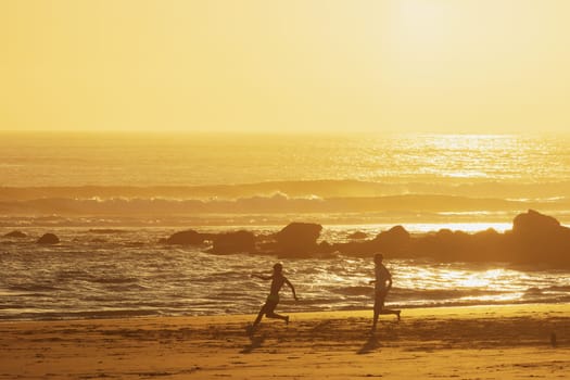Teenage boys playing ball on the beach at sunset. Mid shot