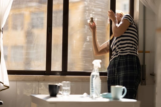 Adult woman housewife washing the outside of a window in the kitchen. Mid shot