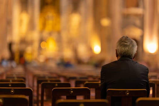 An elderly man sits on a chair in a church. Mid shot