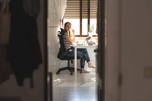 Adult woman freelancer working at the kitchen table - looking in the camera. Mid shot