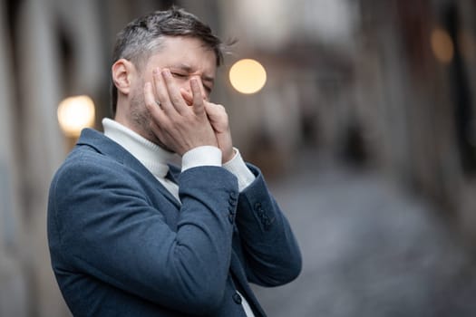 An adult man in blue jacket plays the harmonica on the street. Mid shot