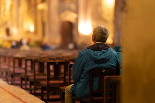 An elderly man sits at the entrance to the church and listens to a sermon. Mid shot