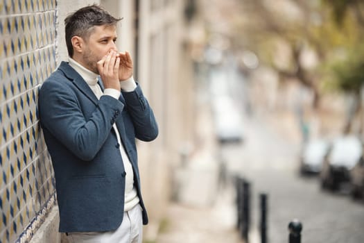 A man stands against the wall and plays the harmonica in the street. Mid shot