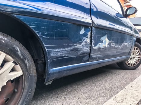 Blue car, dent in a door in the street after a broken accident.  Scratched car body. Dented.