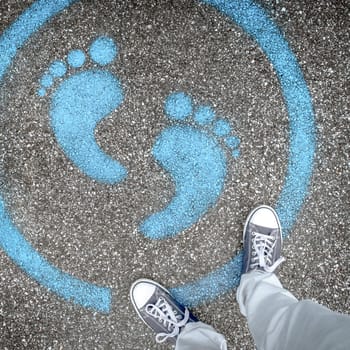Man standing on blue dot. Sign painted on the pavement reminding users to maintain a physical distance of 3 feet / 1 meter during the COVID-19 pandemic.