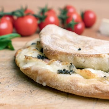 Closed calzone pizza on rustic wooden background. On blurred background small red tomatoes. Italian food. Selective focus