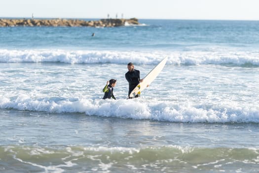 Father and son surfers in wetsuits in the sea. Mid shot