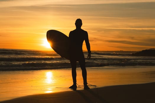 Silhouette of a man surfer holding surfboard on the seashore. Mid shot