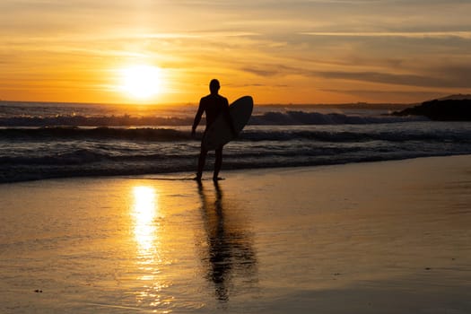 Silhouette of a lonely man surfer holding surfboard on the seashore. Mid shot