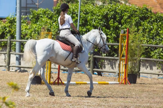 Equestrian sport - a girl in white uniform riding white horse at the ranch. Mid shot