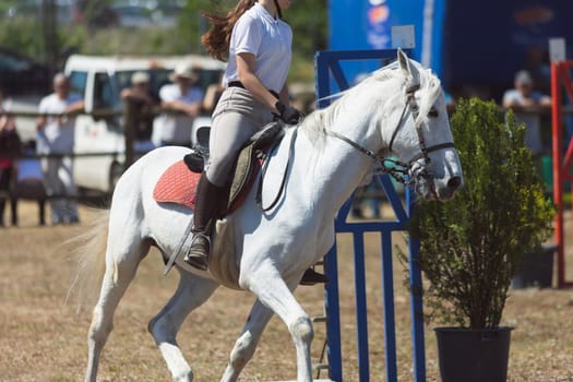 A girl in white uniform riding white horse at the ranch. Mid shot