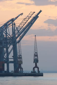 Sea cargo cranes in the port and container terminal of Lisbon, silhouette on sunrise, morning