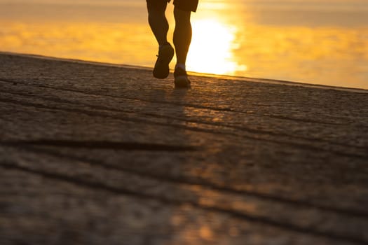 Silhouette of legs athlete running at the sunrise on river coast, jogging