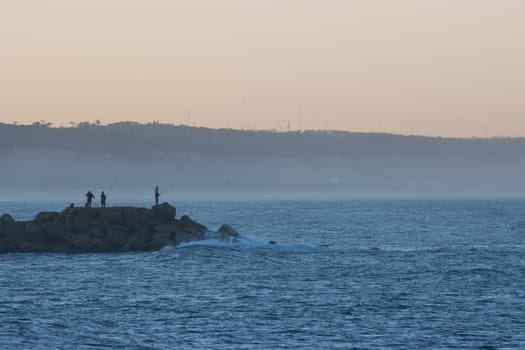 Fishers on the oceans - groupe of men stand on the coast of the sea with fishing rod at sunrise, landscape