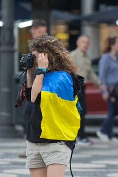 10-29-2022 LISBON, PORTUGAL: Ukrainian protest in Lisbon - a woman with a Ukrainian flag tied around her neck photographs the rally on camera. Mid shot