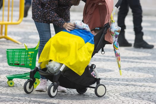 10-29-2022 LISBON, PORTUGAL: Ukrainian protest in Lisbon - a child in a stroller covered with a Ukrainian flag. Mid shot