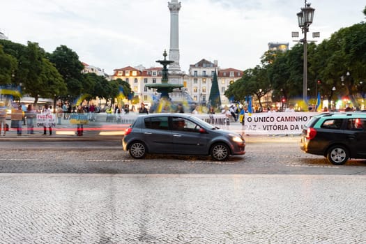 10-29-2022 LISBON, PORTUGAL: Ukrainian protest at Lisbon Square next to the roadway - a car drives past people holding posters. Mid shot
