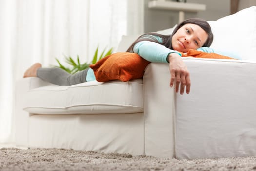 woman easing down on her couch in a white living room
