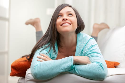 portrait of a relaxed woman on the sofa's armrest cheering with her arms folded and thinking
