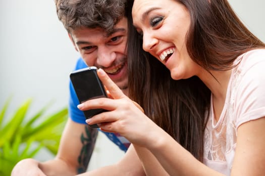 Young couple laughing happily together as they watch media together on her mobile phone in a close up cropped view with focus to their faces