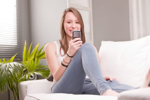 smiling girl using a mobile phone at home in her living room on her sofa
