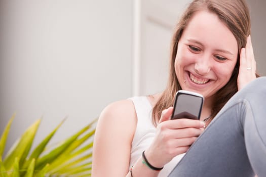 smiling girl using a mobile phone at home in her living room on her sofa