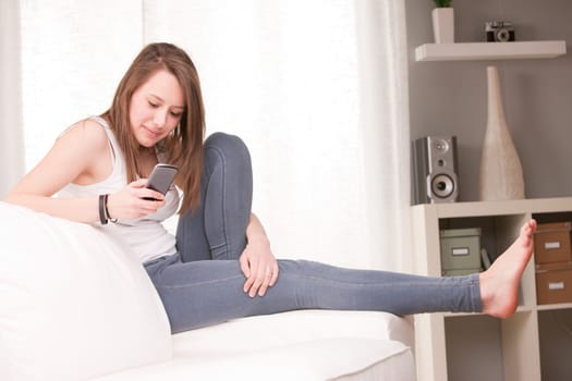 smiling girl using a mobile phone at home in her living room on her sofa