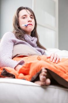 woman with a thermometer in her mouth measuring her temperature as she has enough of this pain in the neck