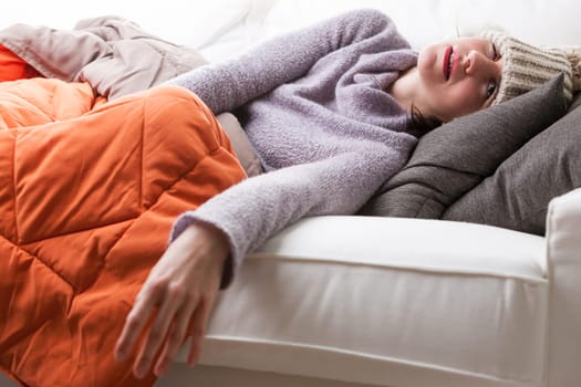 woman lying on a sofa in a pathetic pose with a strong flu and a ridicolous hat