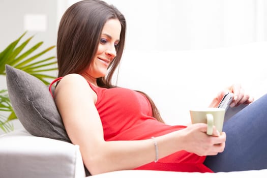 Happy young woman relaxing with coffee and a mobile phone on a comfortable sofa in a close up side view as she smiles quietly to herself