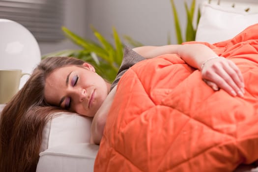 young beautiful sexy woman softly sleeping on her sofa under her warm orange quilt