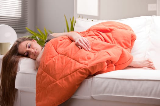 young beautiful sexy woman softly sleeping on her sofa under her warm orange quilt