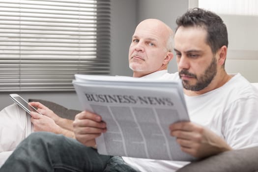 Man sitting reading the Business News in close up with a worried expression watched by an anxious friend or father