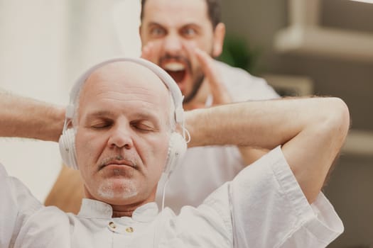 Son yelling at his father who is listening to music on stereo headphones oblivious to his presence