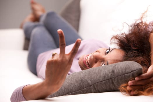 beautiful curly african-american woman lying on a sofa and showing off the winner symbol with her fingers