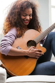young beautiful afroemerican woman having fun with her guitar on her sofa in her living room