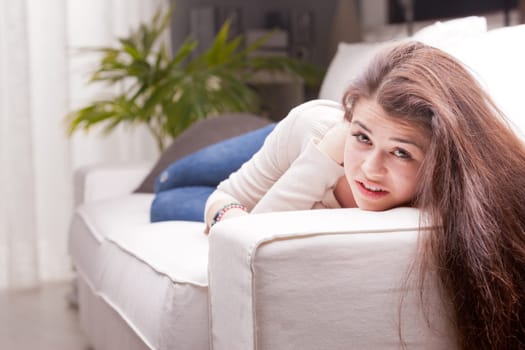pretty girl in blue jeans watching you from a sofa and smiling