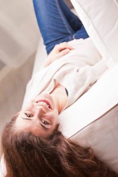 pretty girl in blue jeans watching you from a sofa and smiling