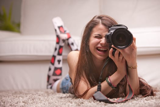 pretty girl taking photographs with a professional digital camera with a playful spirit at home