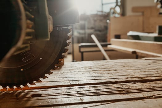 Close up on the blade of a circular power saw in a workshop backlit by a bright sunburst through a window