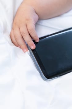 Conceptual image of a newborn baby and mobile phone with its tiny fingers touching the screen as it lies on a white bed